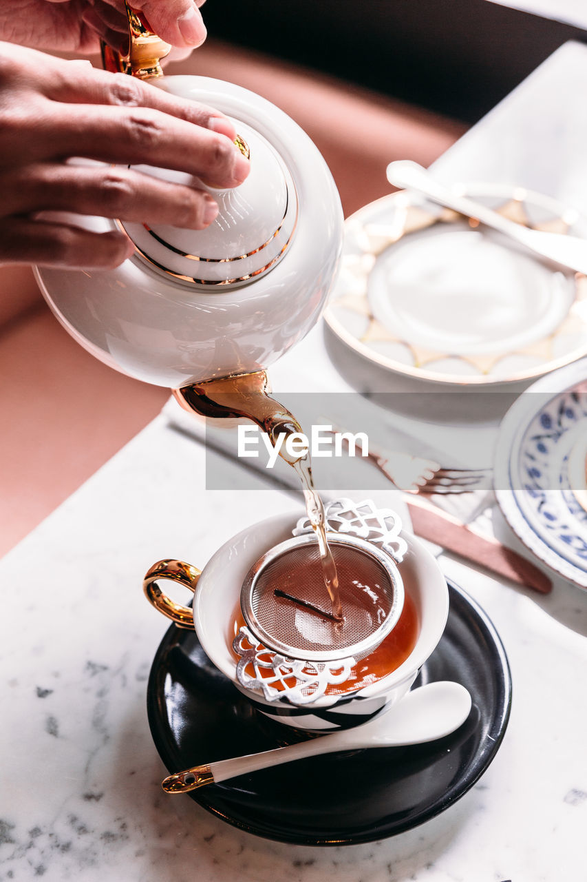 High angle view of cropped hand pouring tea from kettle in cup on table