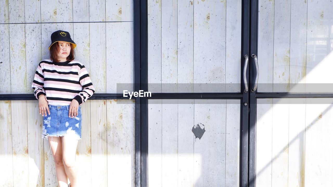 Portrait of young woman standing against wall