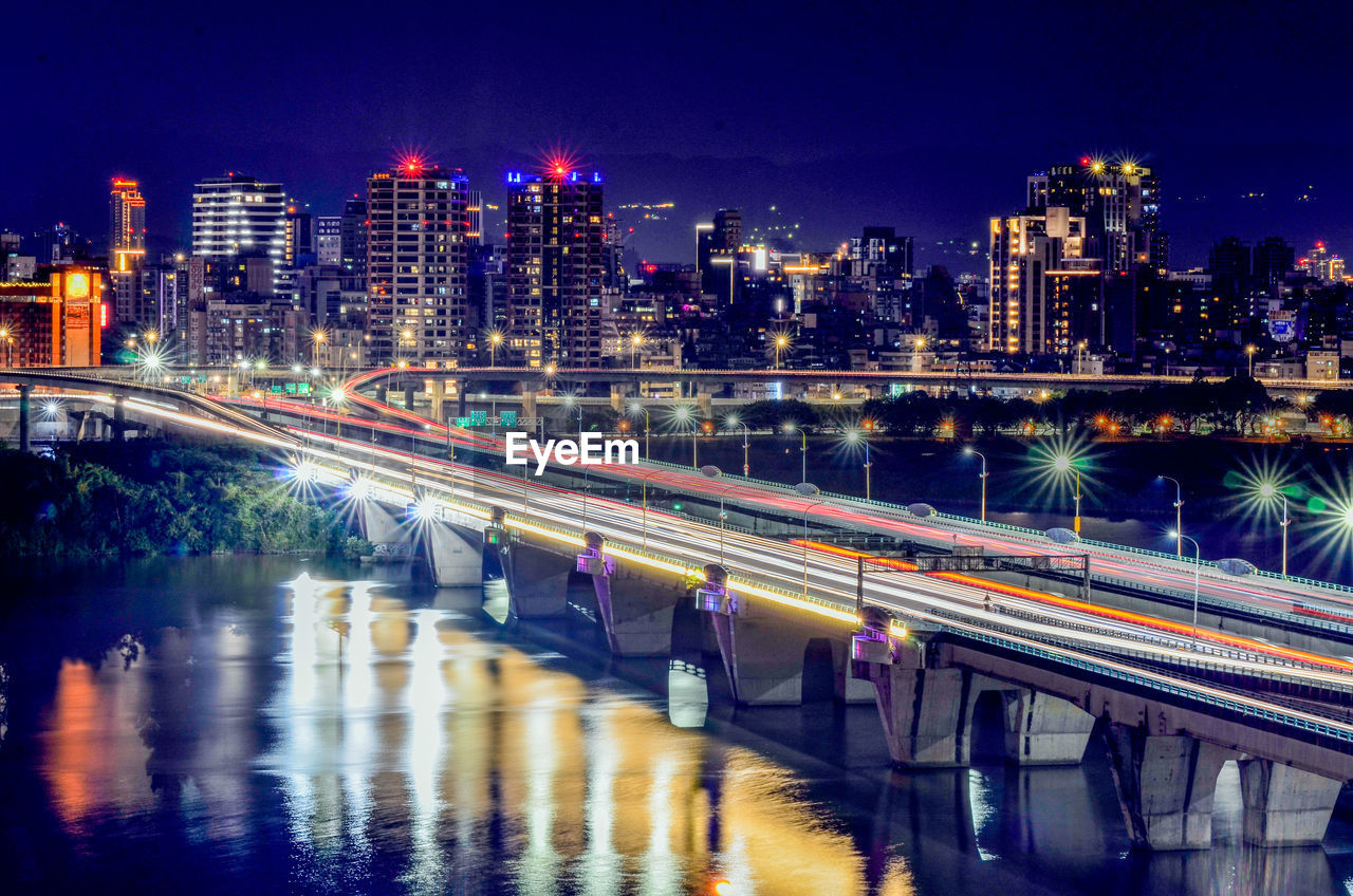 Light trails on bridge over river in city at night