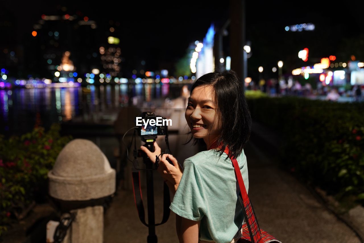 Portrait of smiling woman photographing from camera in city at night