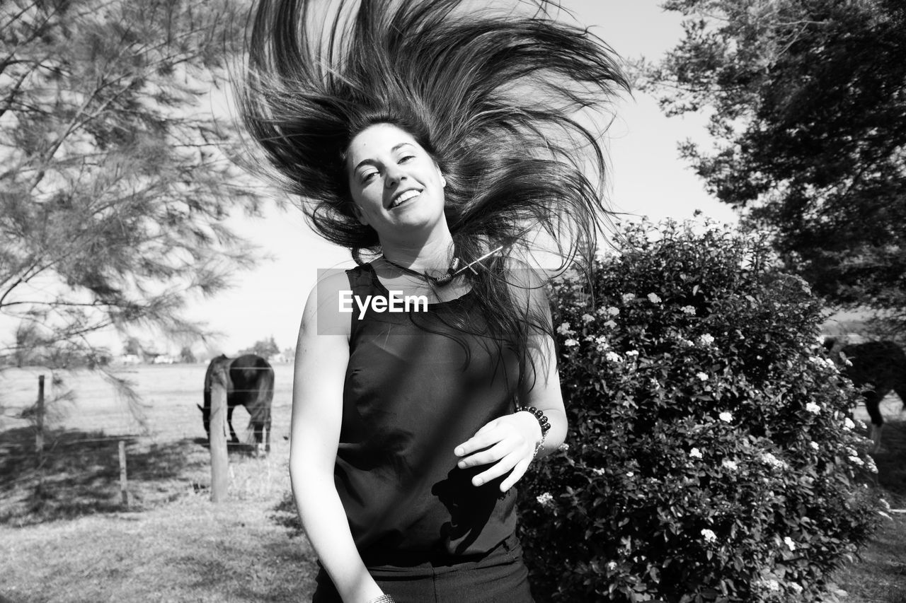 Portrait of smiling woman tossing hair while standing by plant