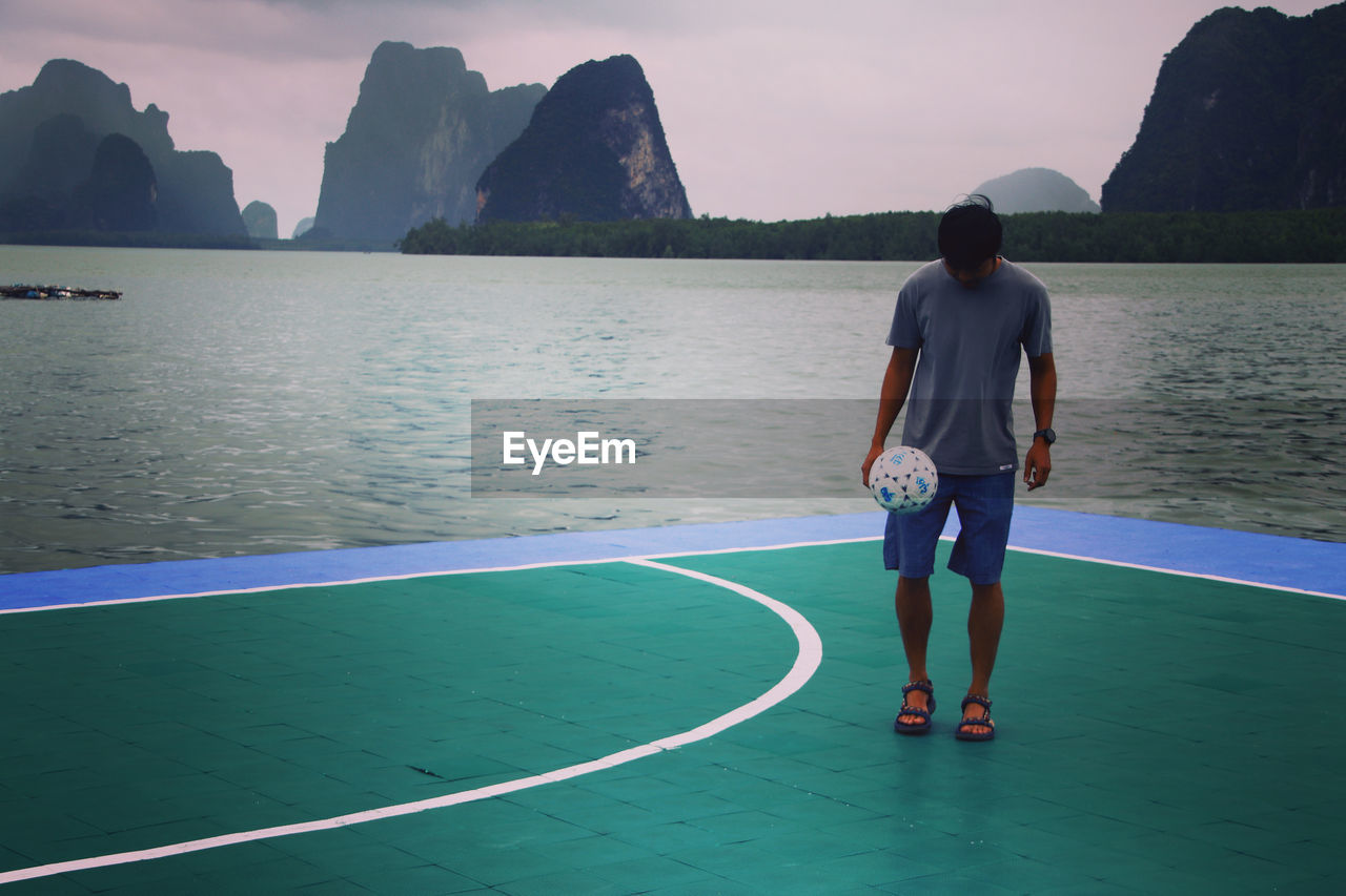 FULL LENGTH REAR VIEW OF MAN STANDING ON SEA SHORE AGAINST SKY