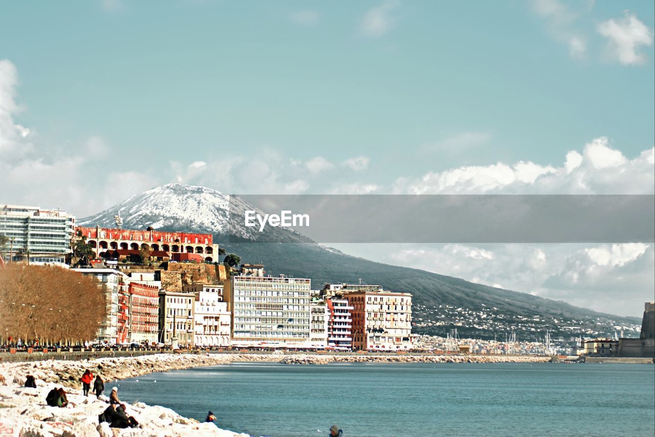 Buildings by sea against cloudy sky