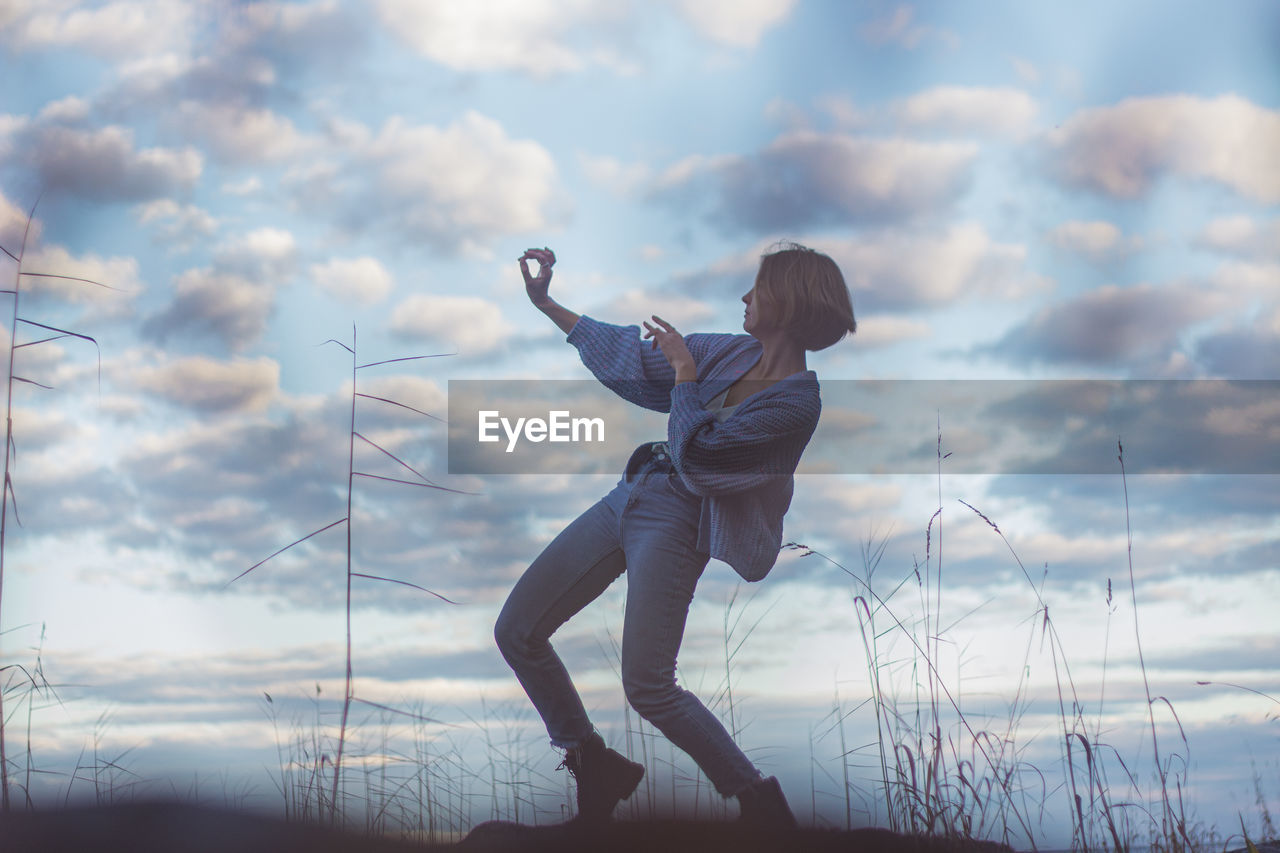 Young woman dancing on rock against cloudy sky