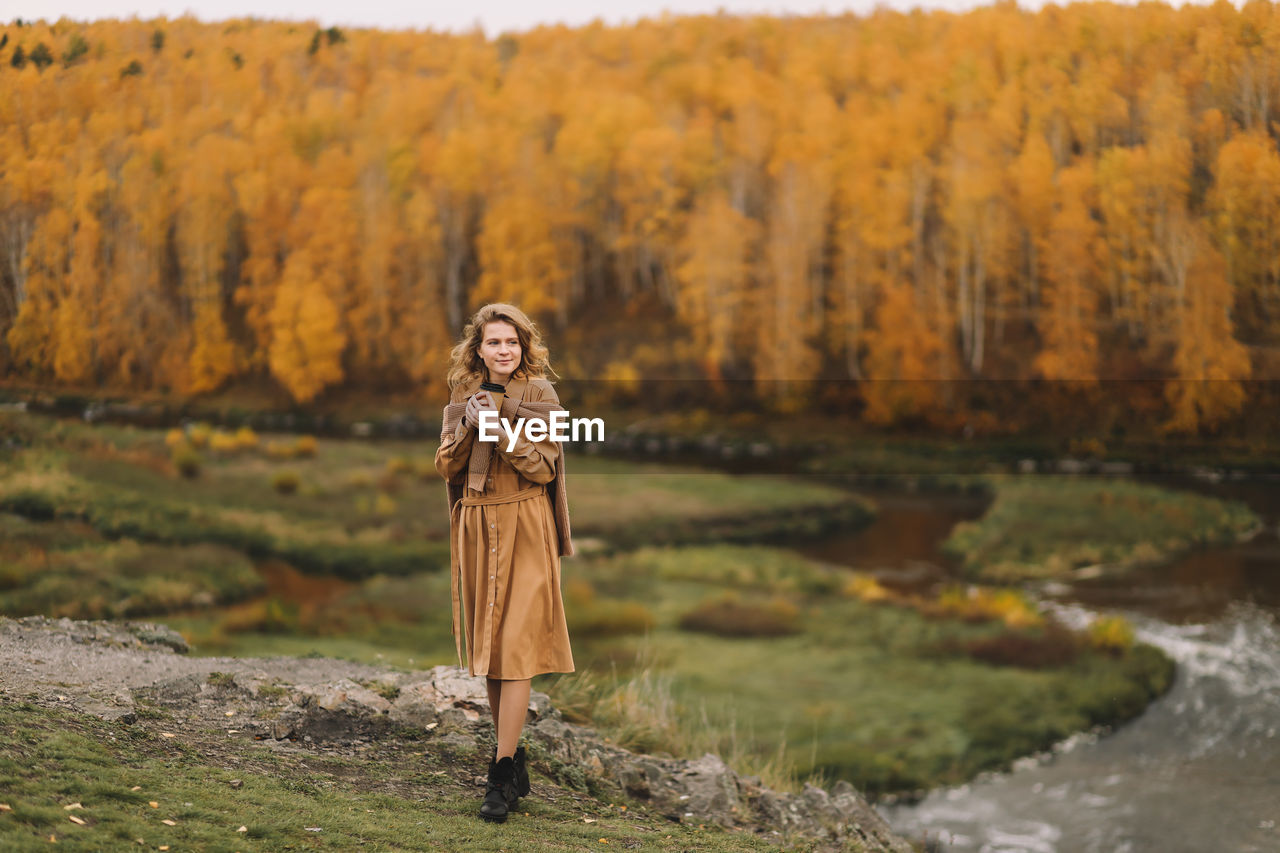 A pretty girl enjoys solitude drinks coffee walks in the autumn forest in nature in fall