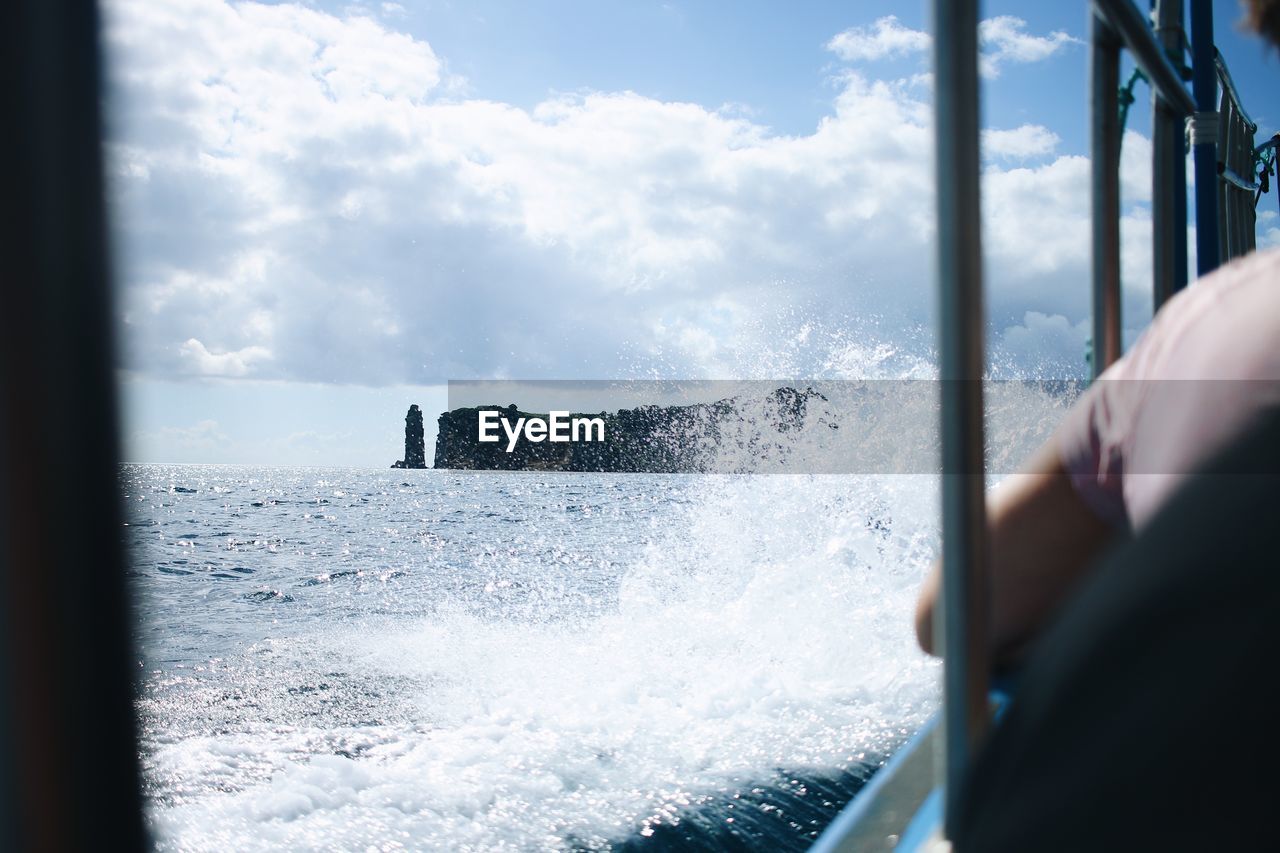 Cropped hand of person sitting in boat against sky