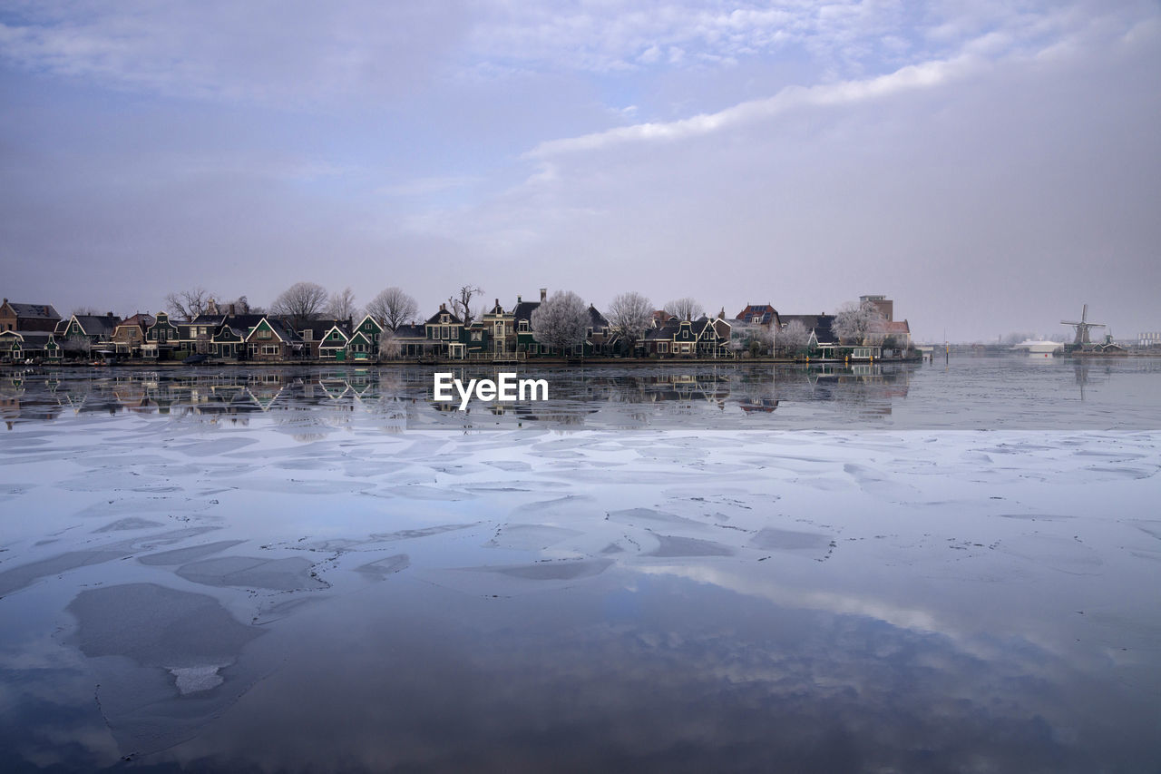 View of frozen lake by buildings against sky