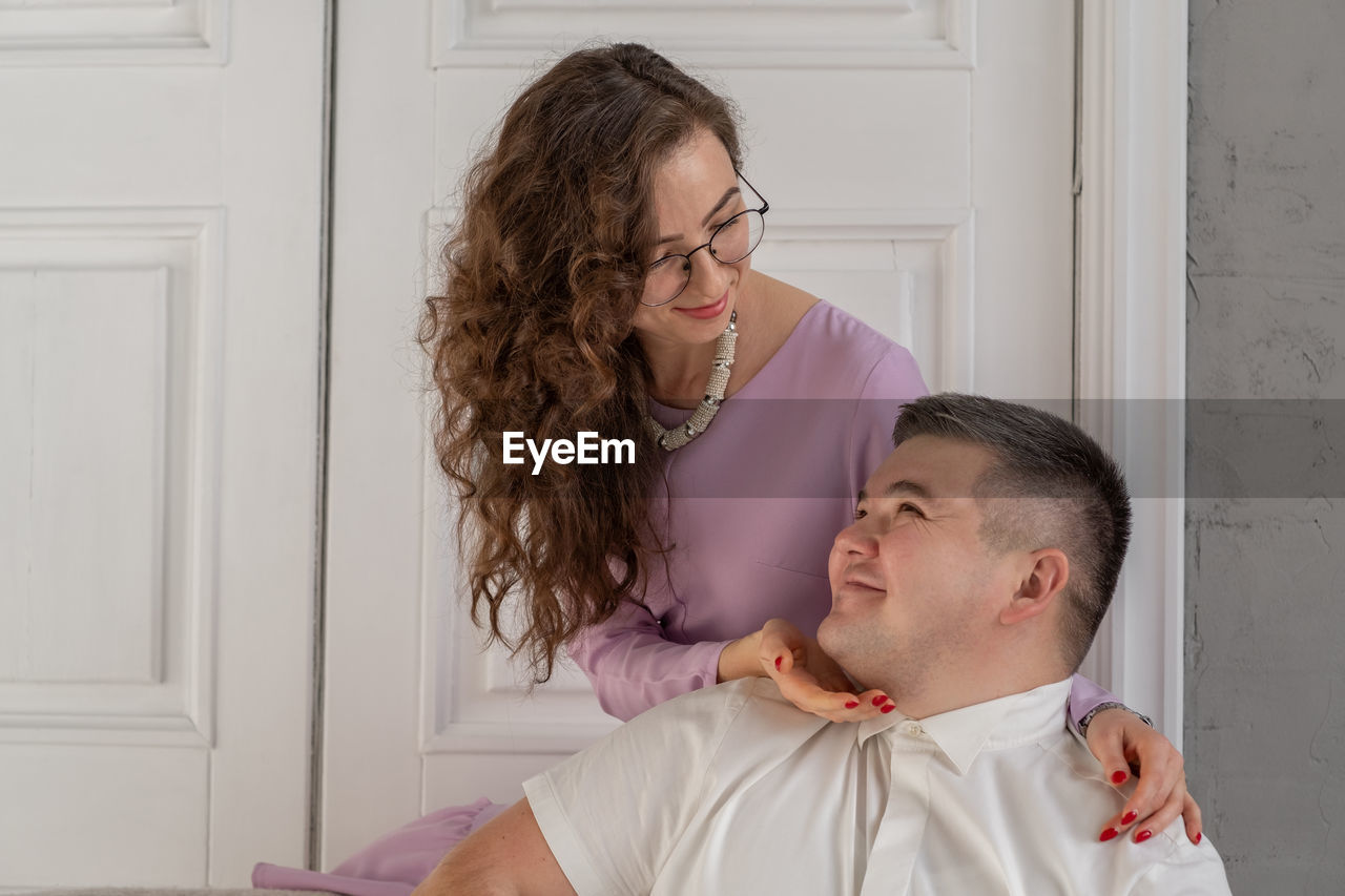 Young happy couple sitting on a sofa in a large studio. behind them is a large white door. 