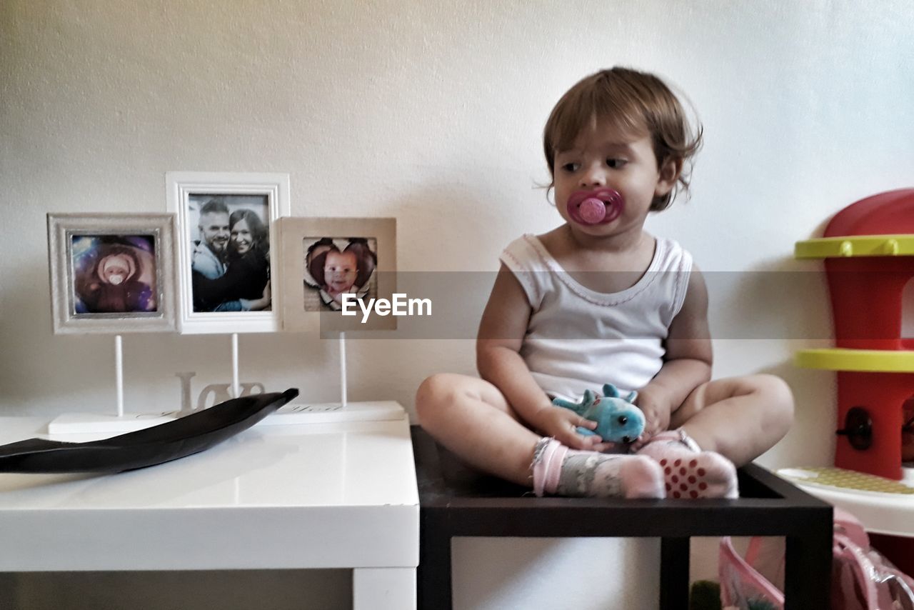 Cute girl sucking pacifier while sitting on table at home