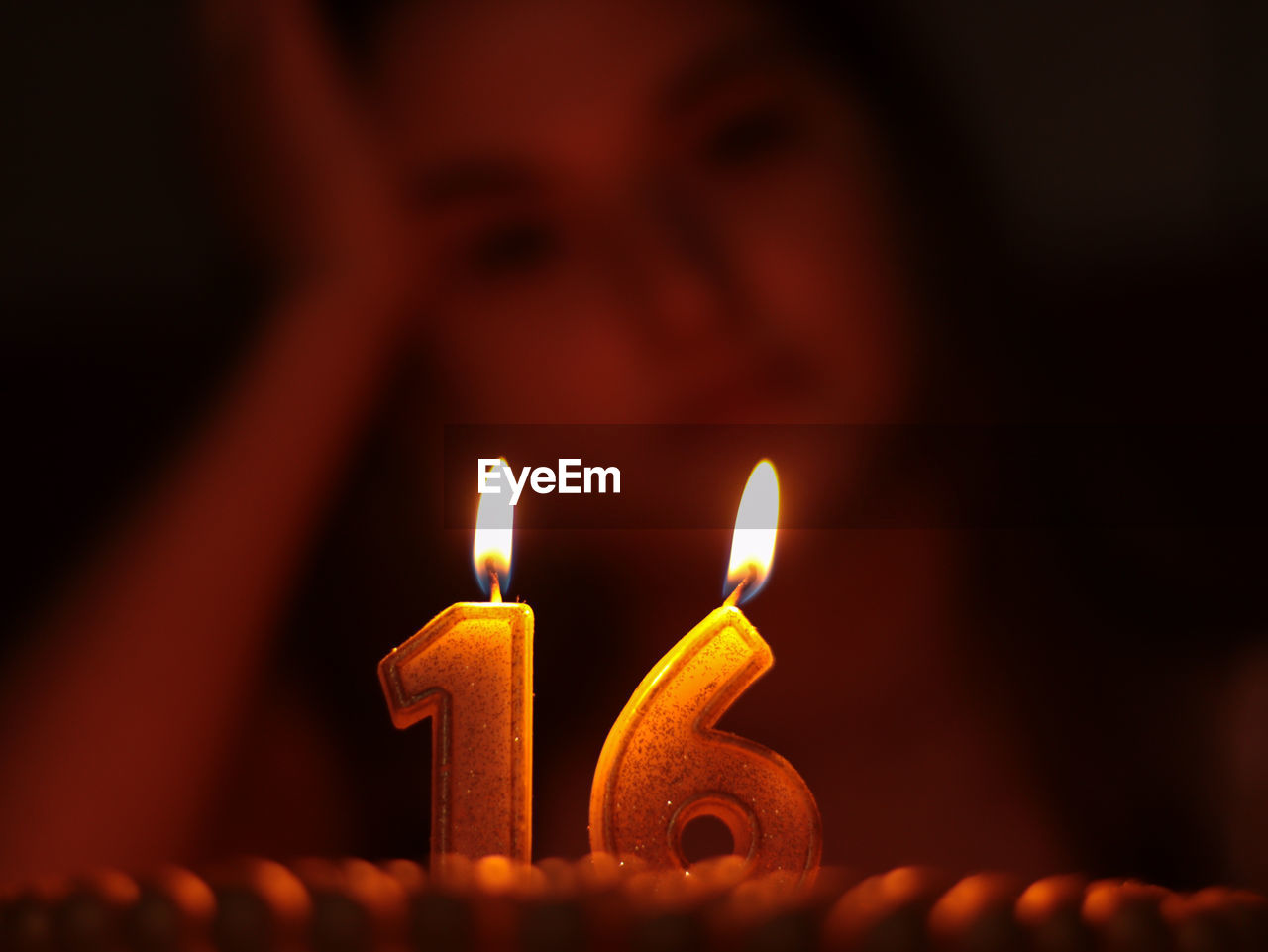 Close-up of teenage girl with illuminated candles on birthday cake in darkroom