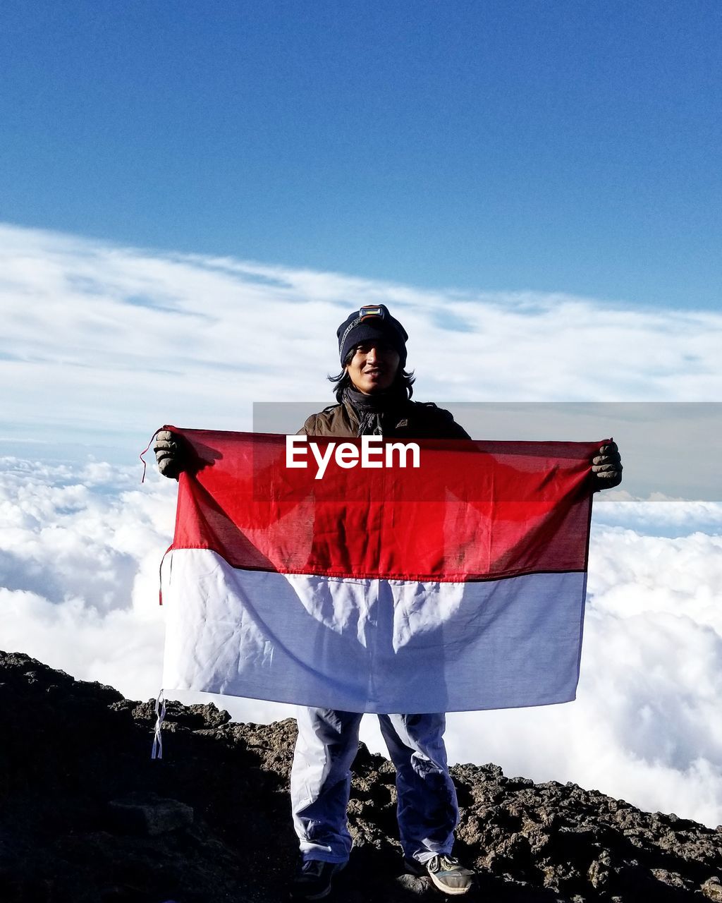 Portrait of young man holding indonesian flag against cloudscape