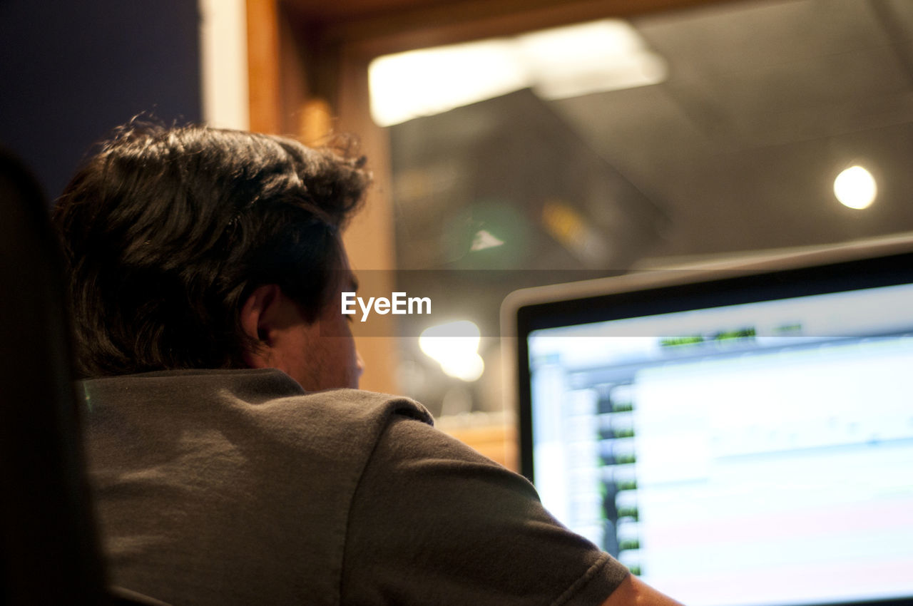 Rear view of man using computer in illuminated recording studio