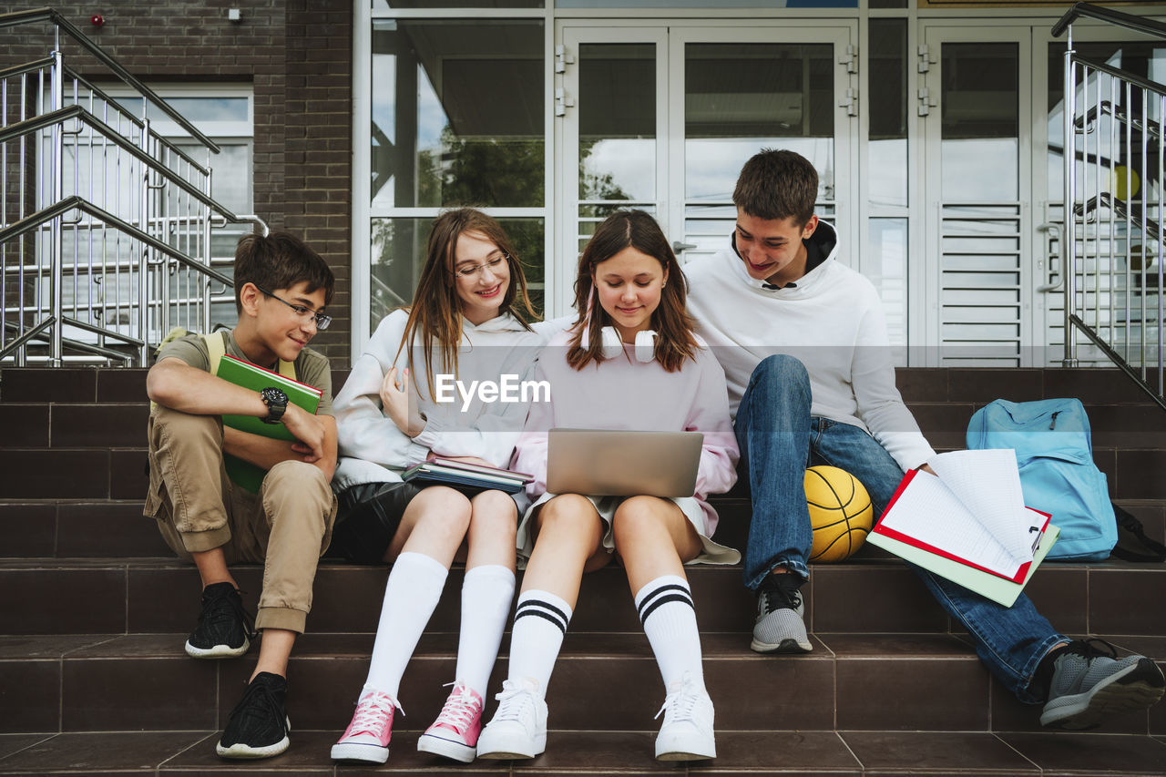 Girl doing homework over laptop by friends sitting on steps at school