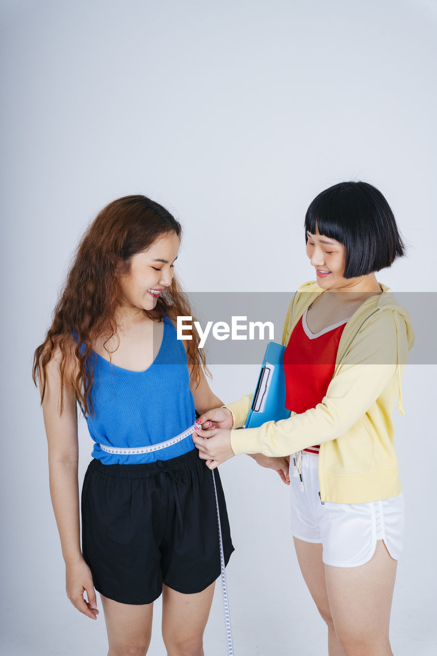 Woman measuring waist of partner against gray background