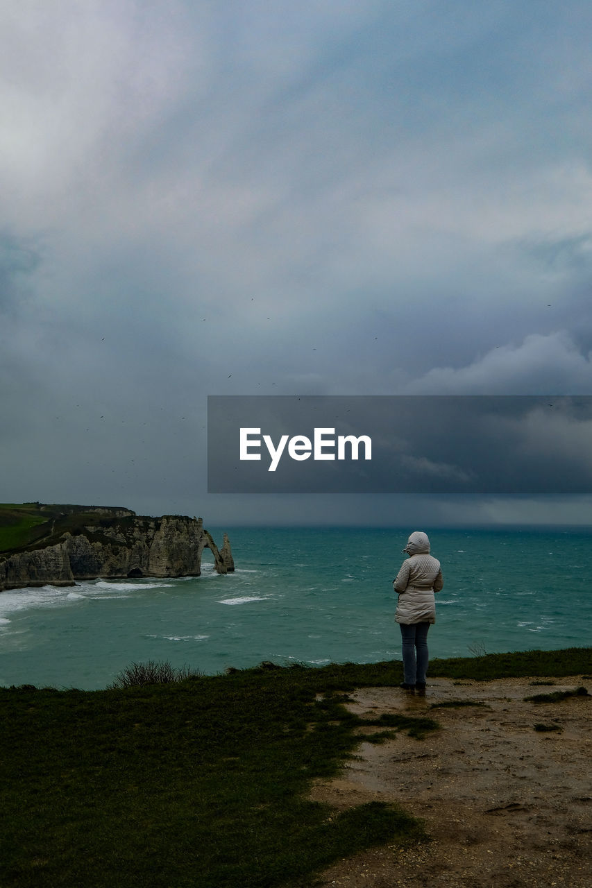 Woman standing at beach against cloudy sky