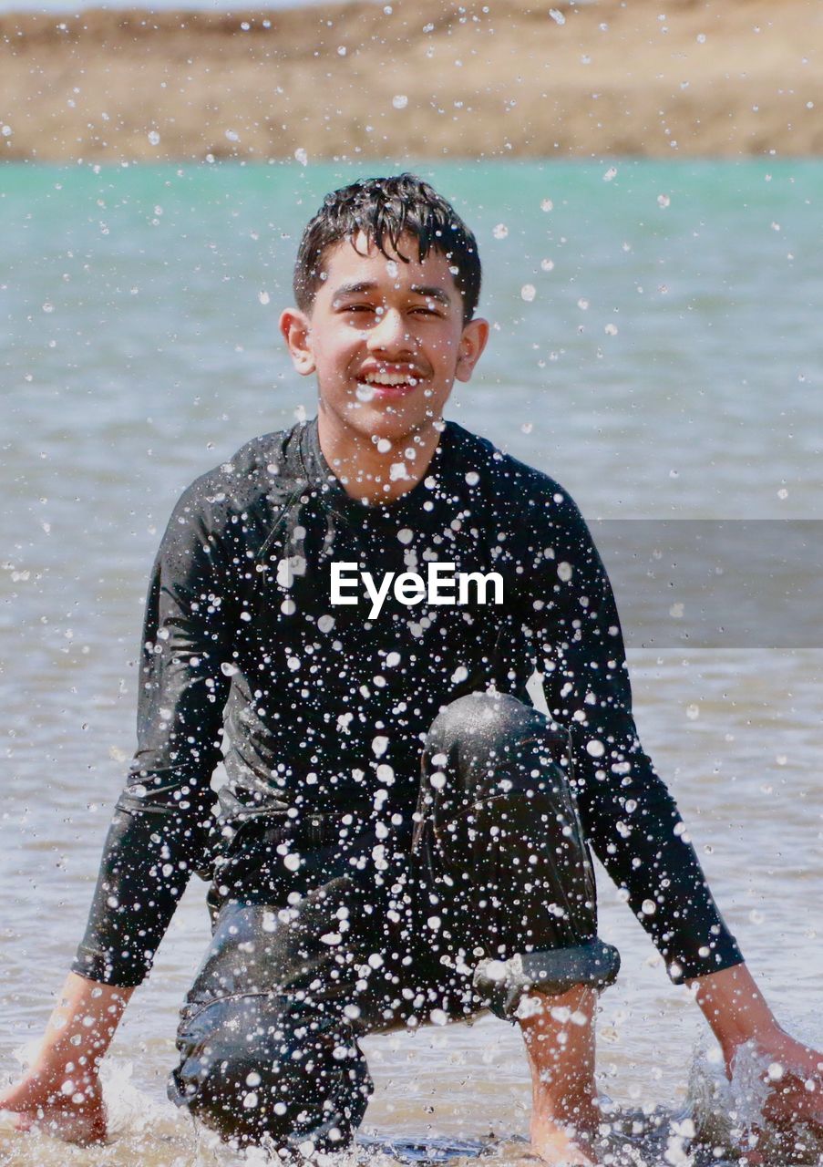 Smiling teenage boy crouching on shore at beach