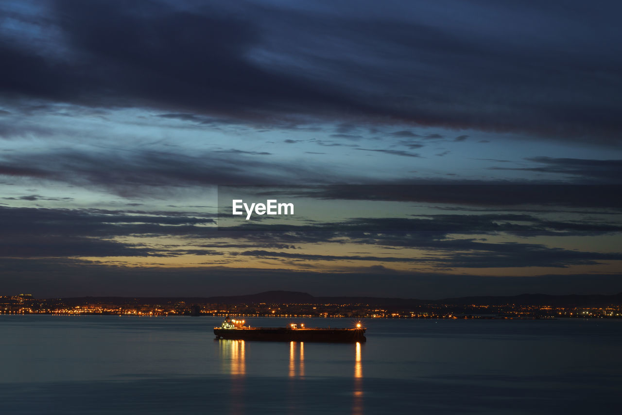 Illuminated boat on sea against cloudy sky at dusk