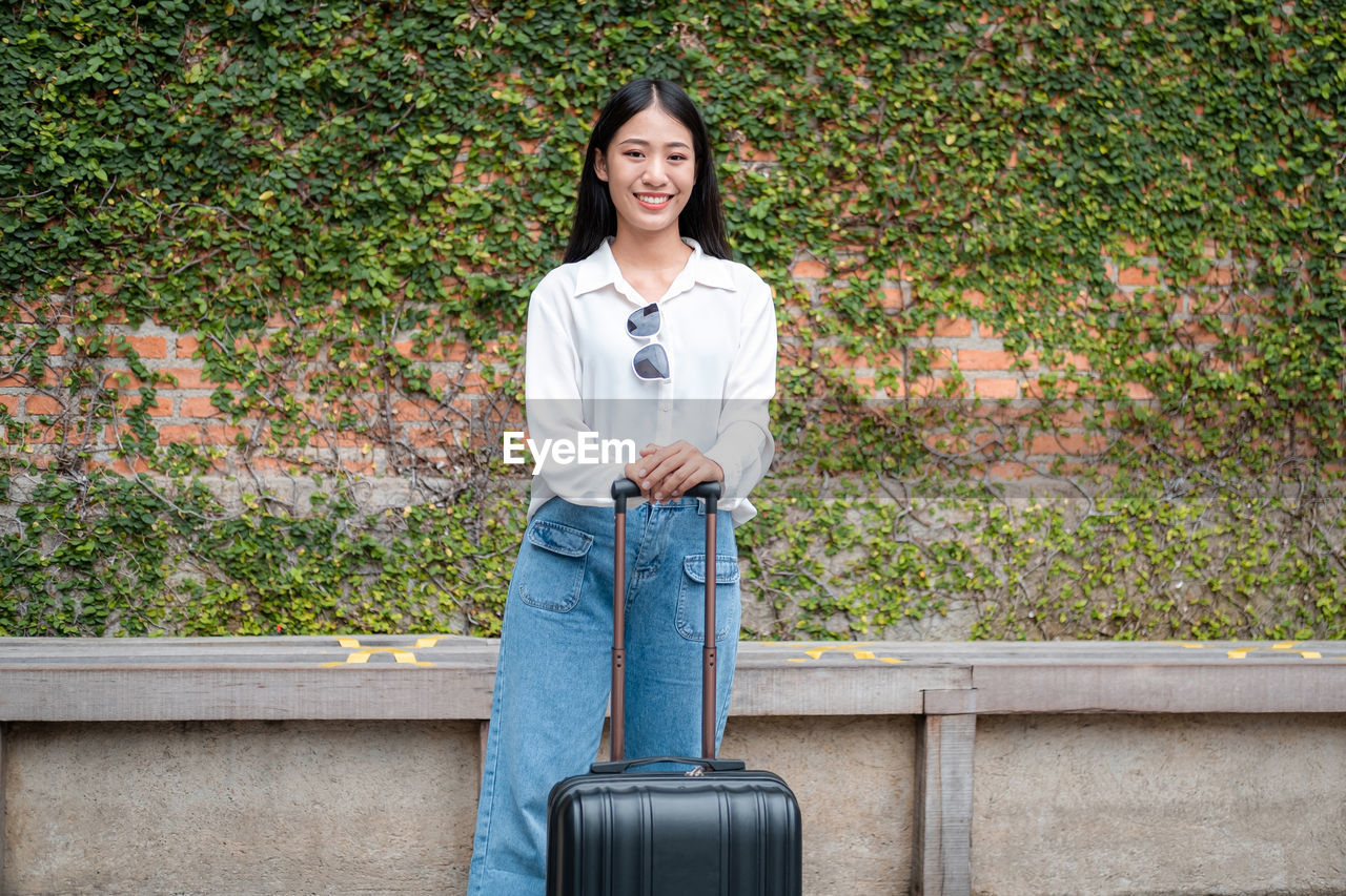 portrait of smiling young woman standing against plants