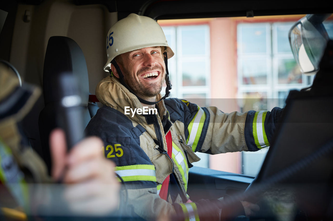 Smiling firefighter looking at coworker while sitting in fire engine