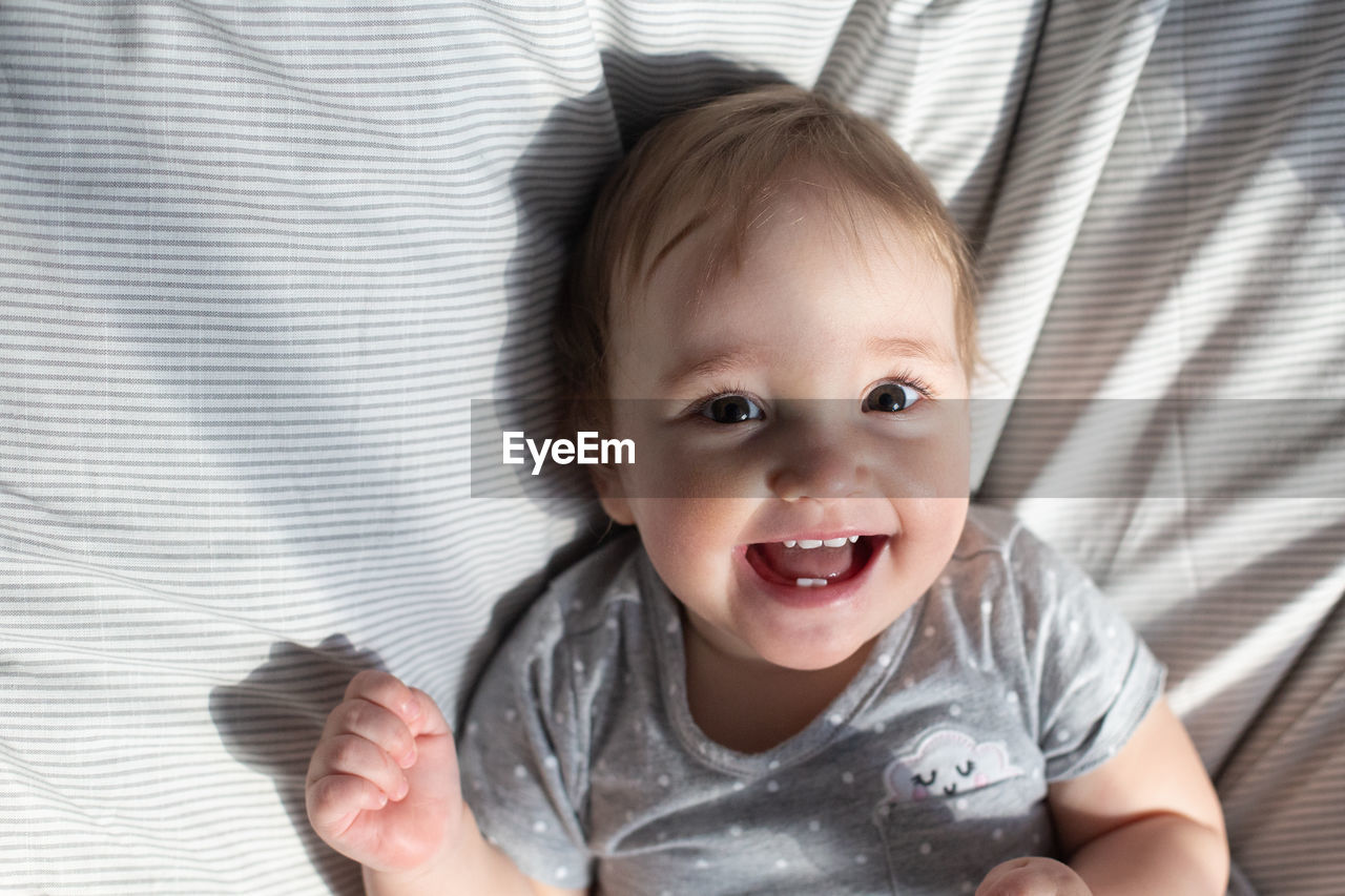 Cute smiling baby girl laying in the bed in morning sun light. grey colors