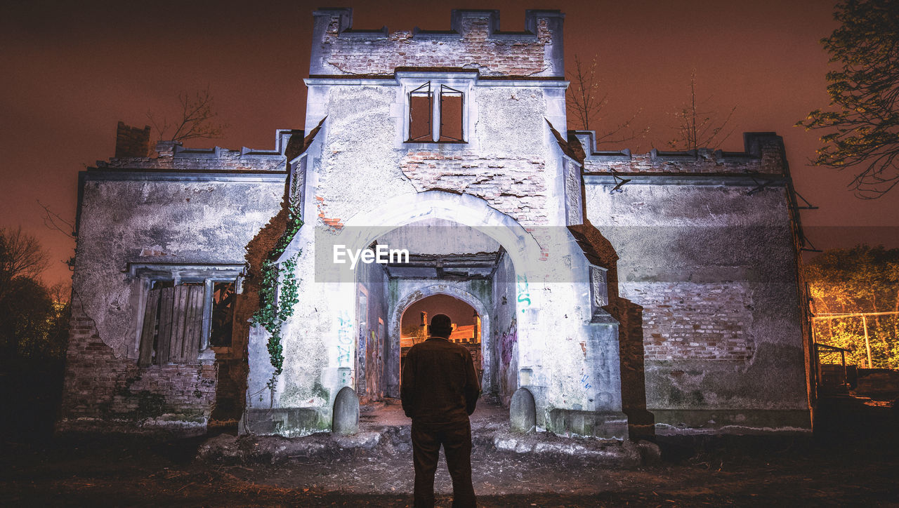 Rear view of man standing against illuminated building at night