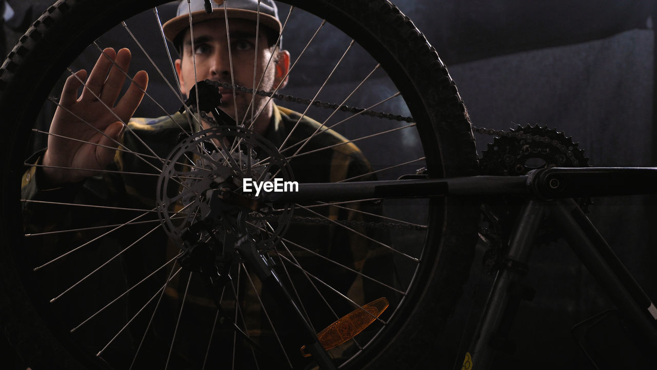 A bike mechanic wearing a baseball cap and shirt repairs a bicycle in a workshop a man spins a wheel