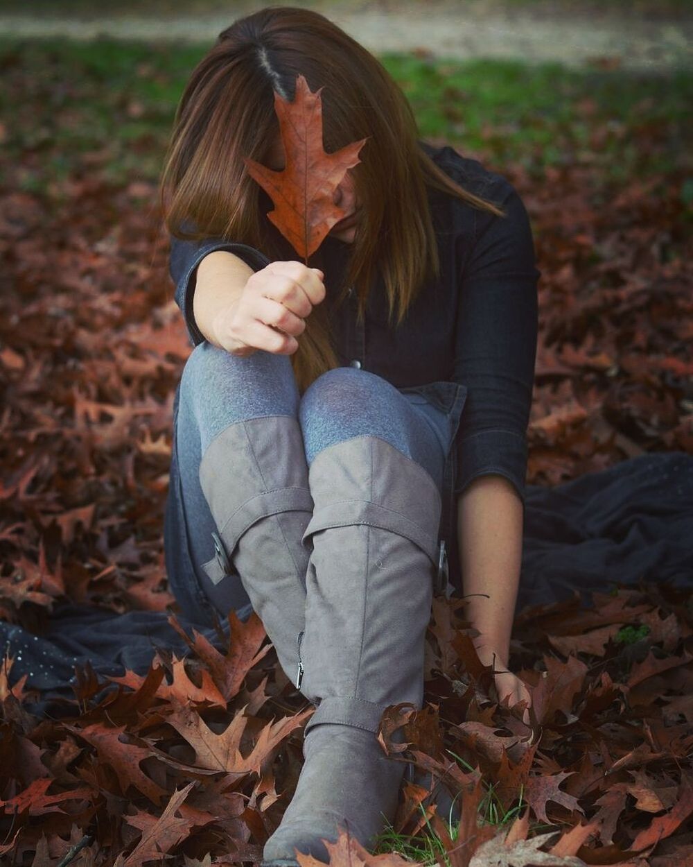 Full length of woman showing autumn leaf while sitting on field
