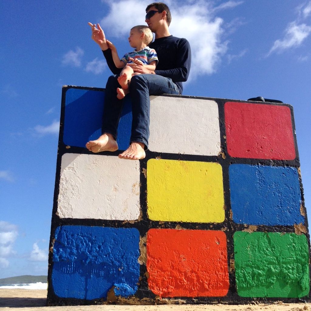 Low angle view of father and son sitting on graffiti painted rock against sky