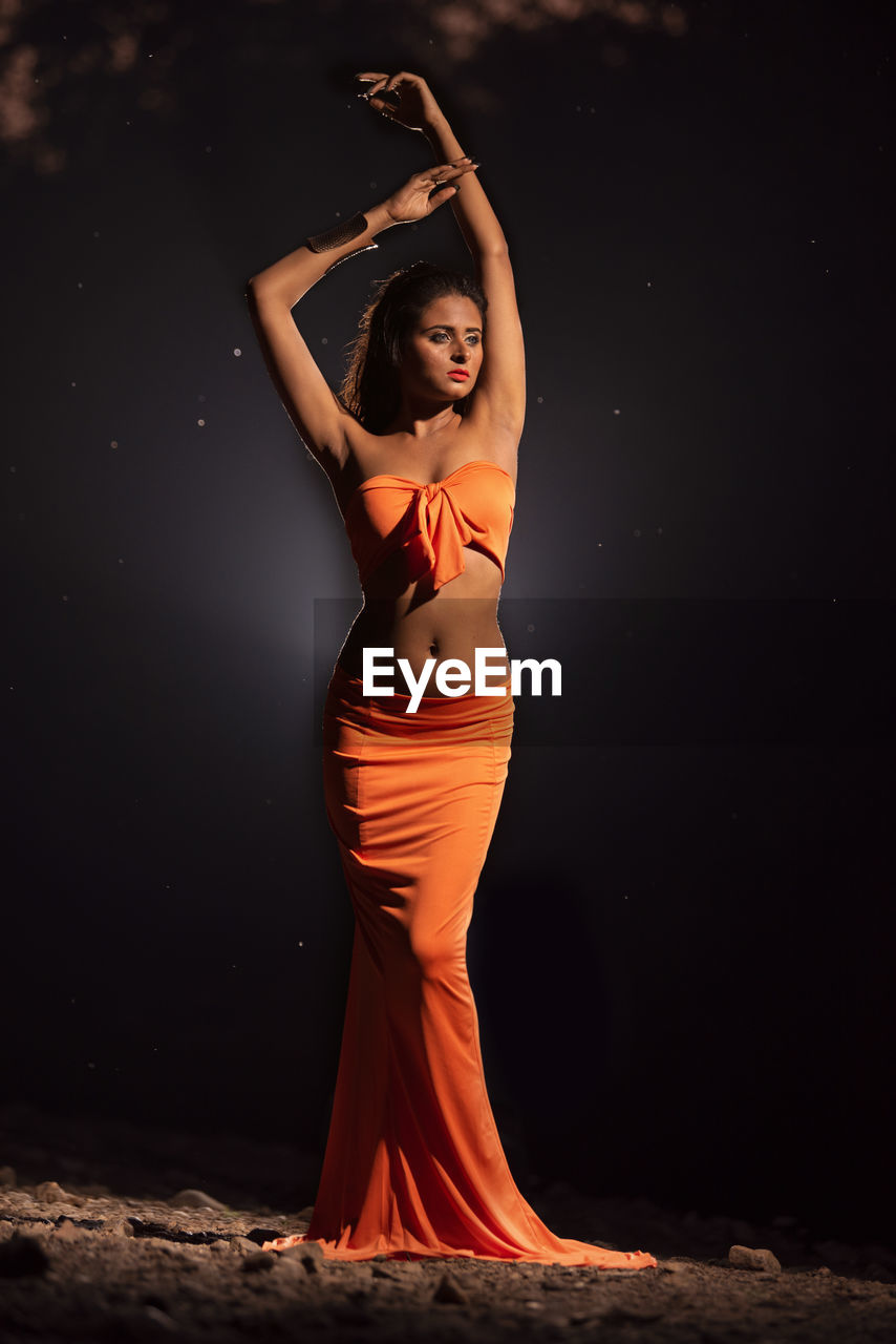 YOUNG WOMAN STANDING AGAINST BLACK BACKGROUND AT NIGHT