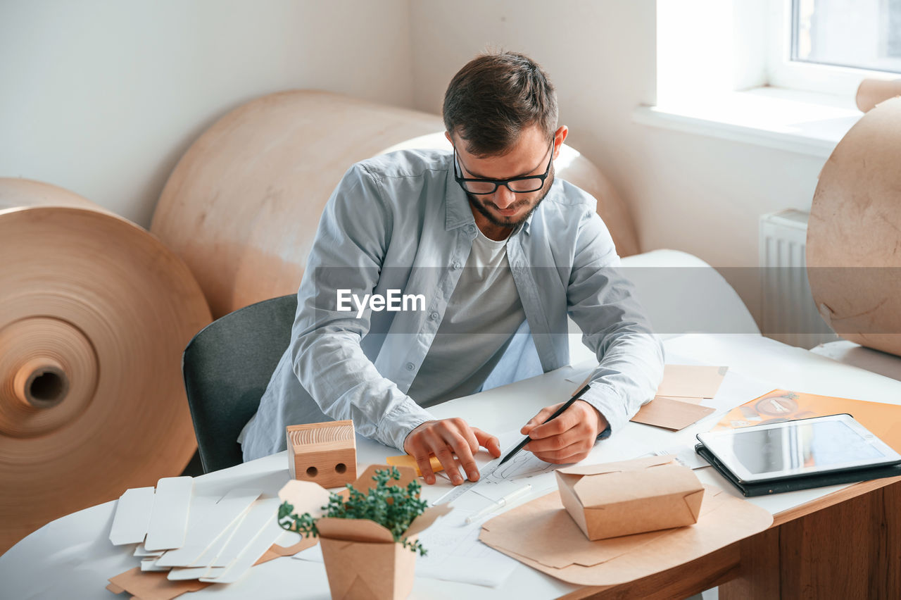 adult, technology, men, business, indoors, one person, wireless technology, business finance and industry, working, furniture, communication, table, businessman, computer, businesswear, sitting, occupation, office, person, glasses, creativity, eyeglasses, desk, home interior, lifestyles, looking, looking down, new business, clothing, young adult, laptop, internet, digital tablet, using laptop, small business, casual clothing, concentration, beard, portability, place of work, computer network, finance, professional occupation, entrepreneur, document, paper