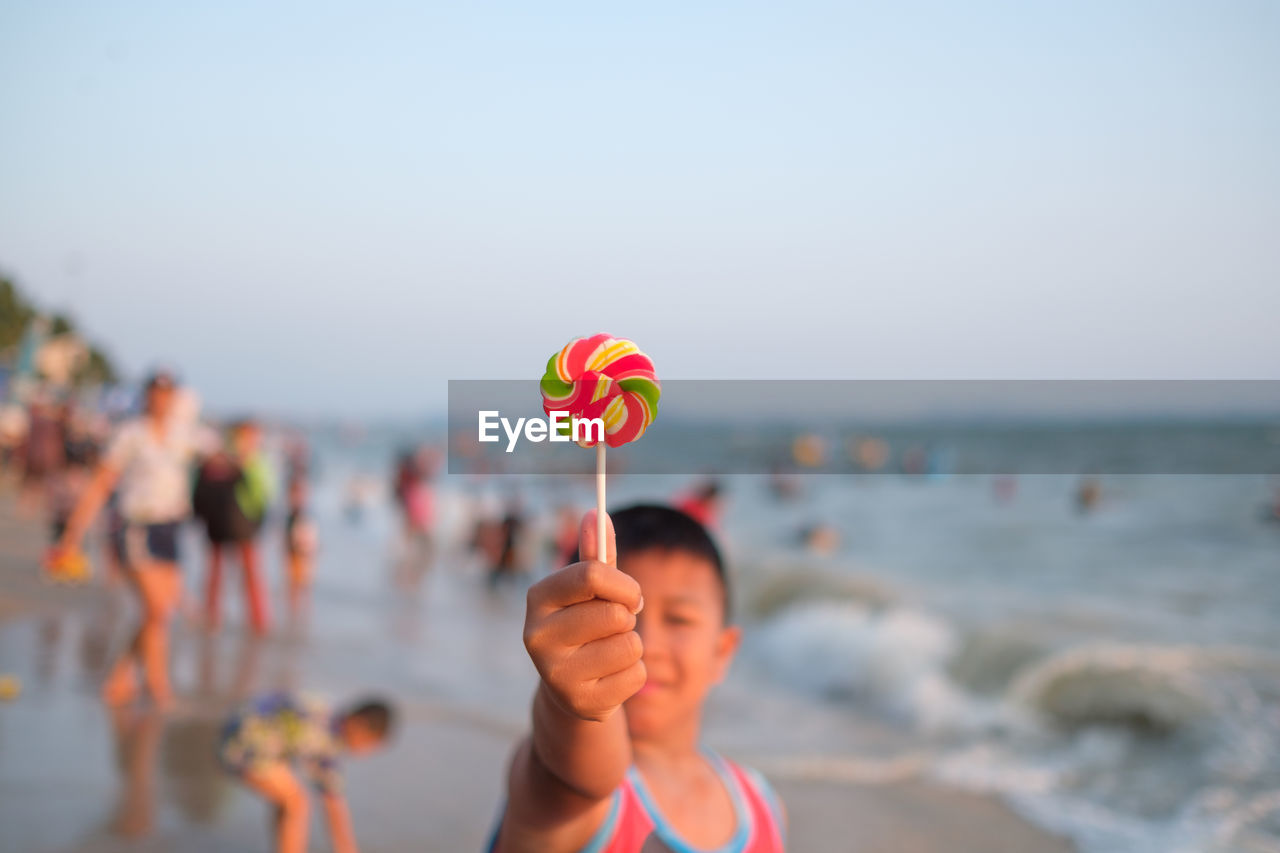 Boy holding lollipop at beach against sky