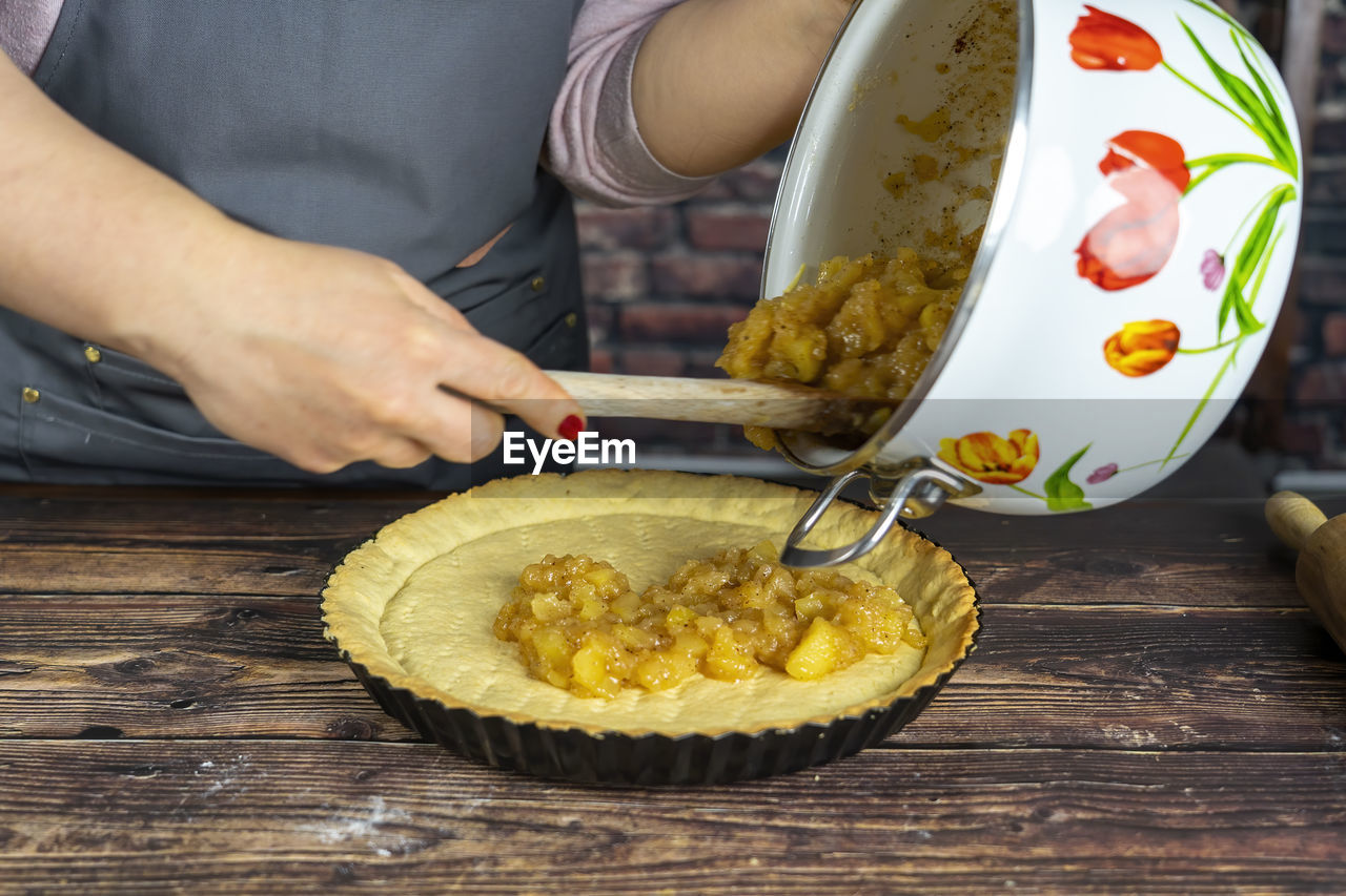 Women preparing delicious apple tart or pie .spreading the cooked candied apple over the dough