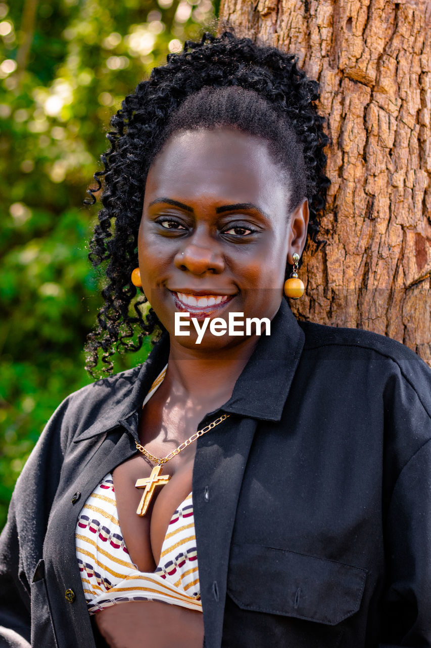 Portrait of smiling mid adult woman standing against tree trunk