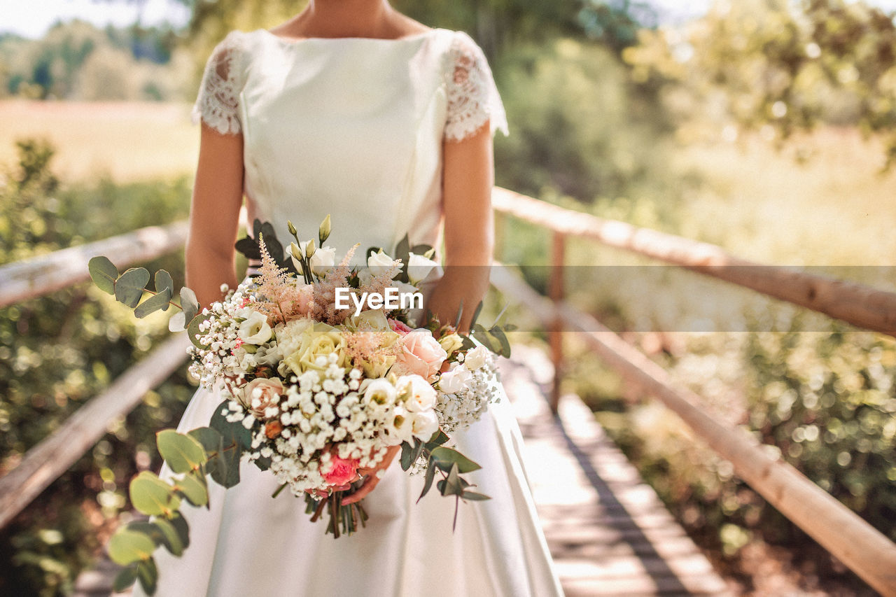 Midsection of bride holding flower bouquet in park