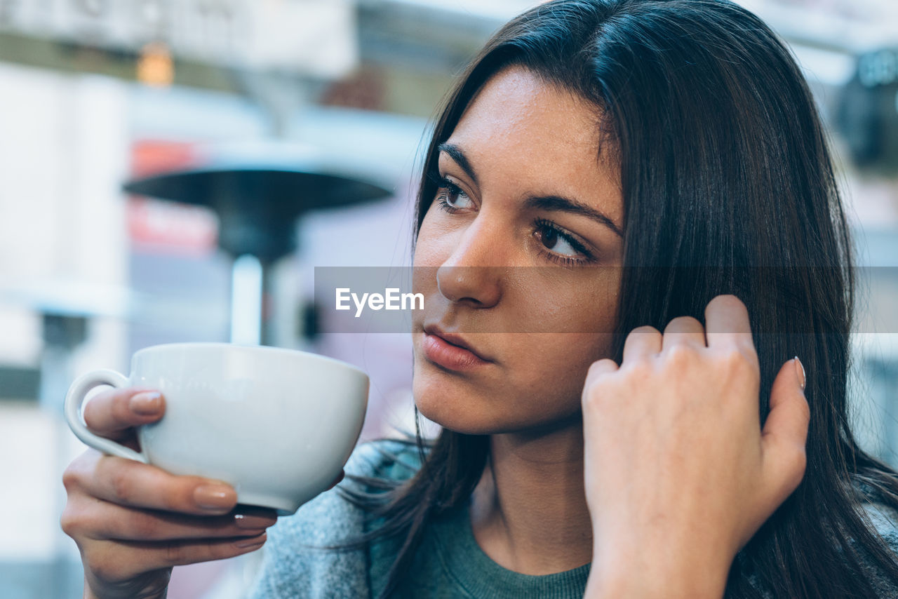 Close-up of thoughtful woman having coffee at sidewalk cafe