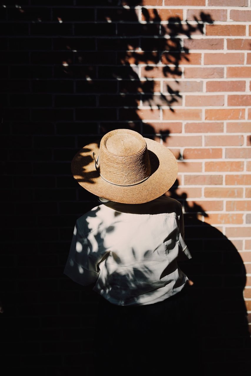 Rear view of person wearing sun hat against brick wall