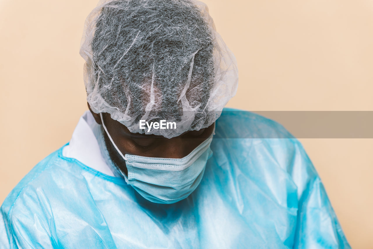 Doctor wearing mask sitting against colored background