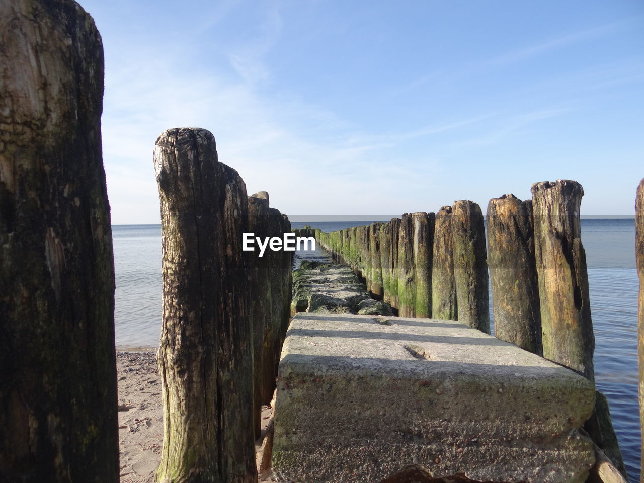 Narrow wooden posts in calm sea against blue sky