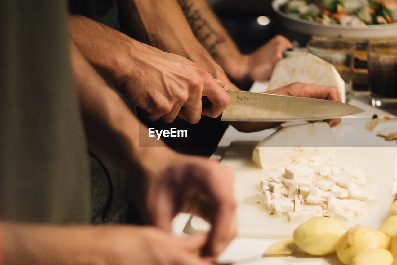 Midsection of men chopping vegetables on cutting board at kitchen