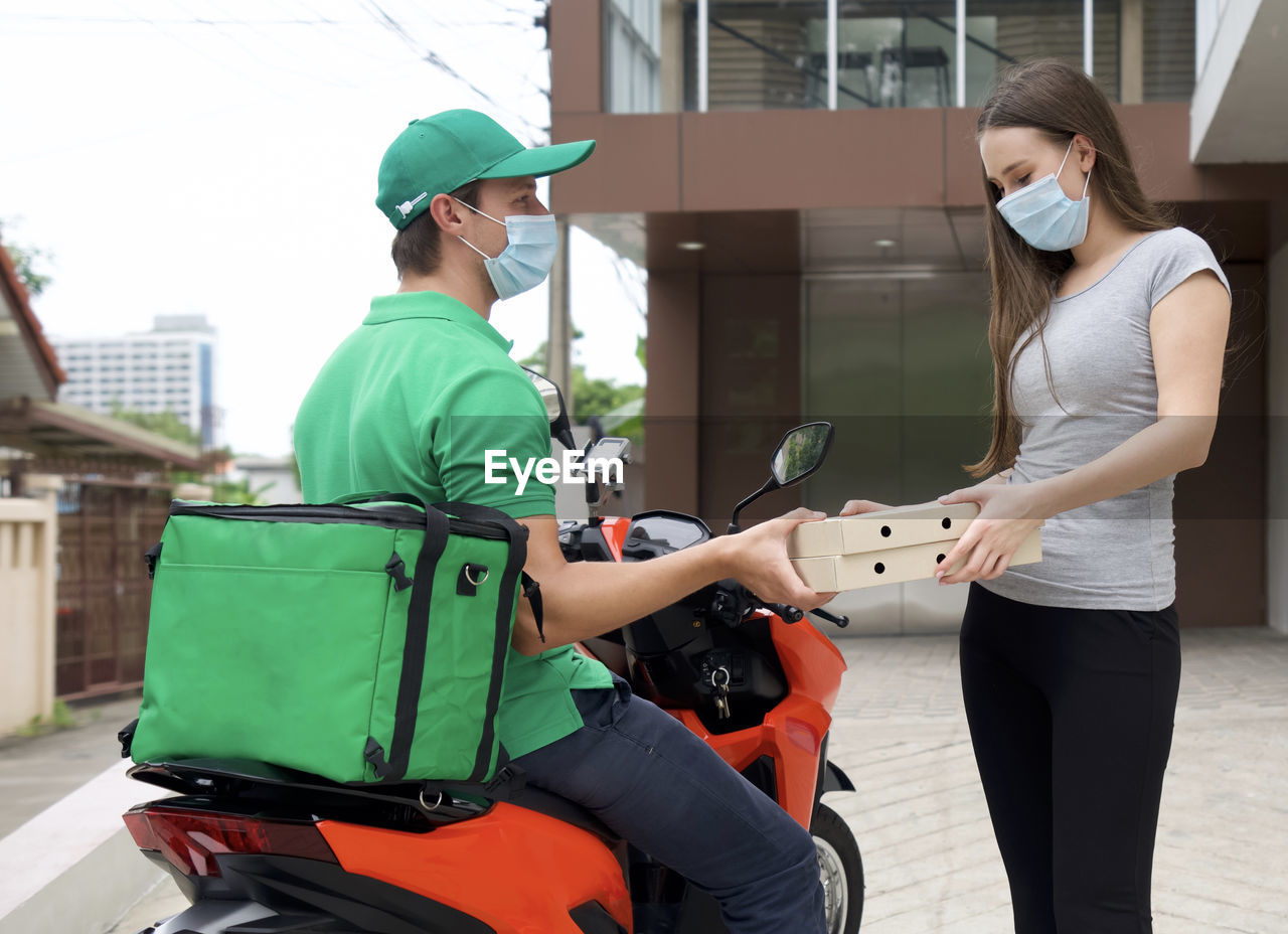 Delivery person wearing mask giving parcel to woman outside home