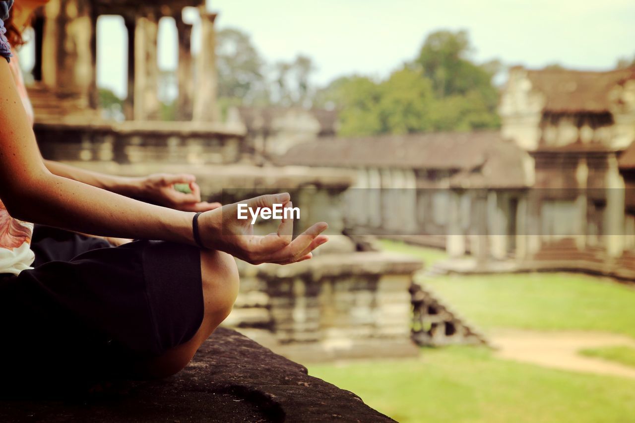 Cropped image of woman doing yoga by artificial pond