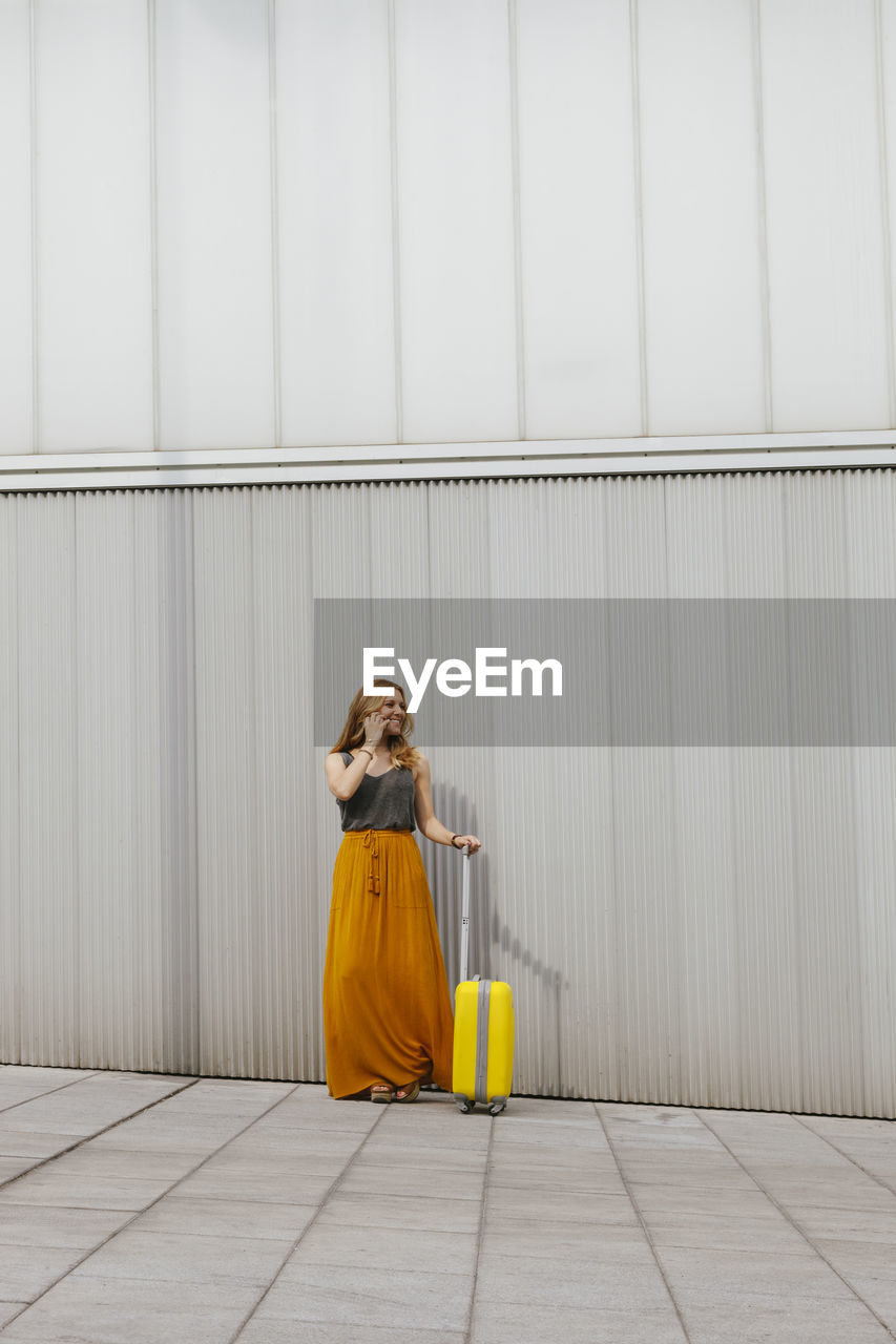 Full length of woman with luggage standing by wall