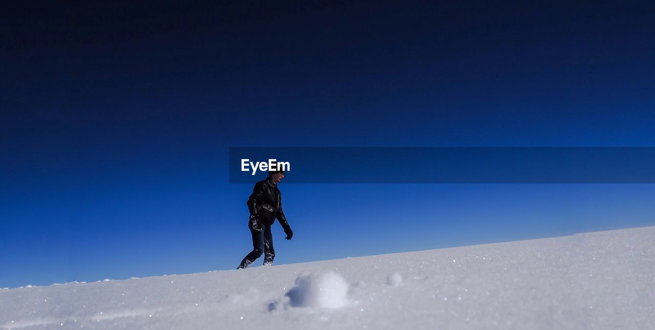 Low angle view of man walking on snow against clear blue sky