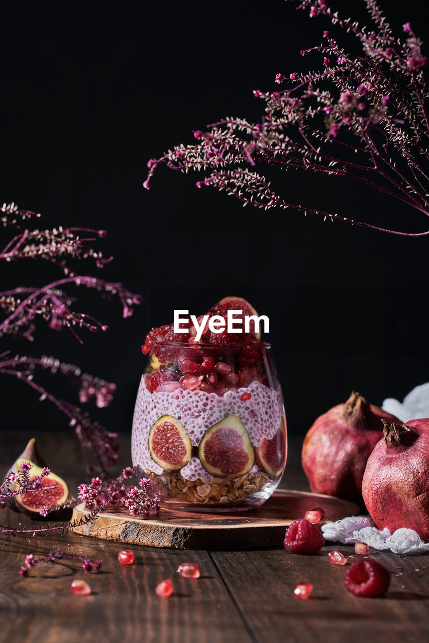 Side view of fresh fruit jam in small jar with full and cut figs on plate at black kitchen table next to pomegranates