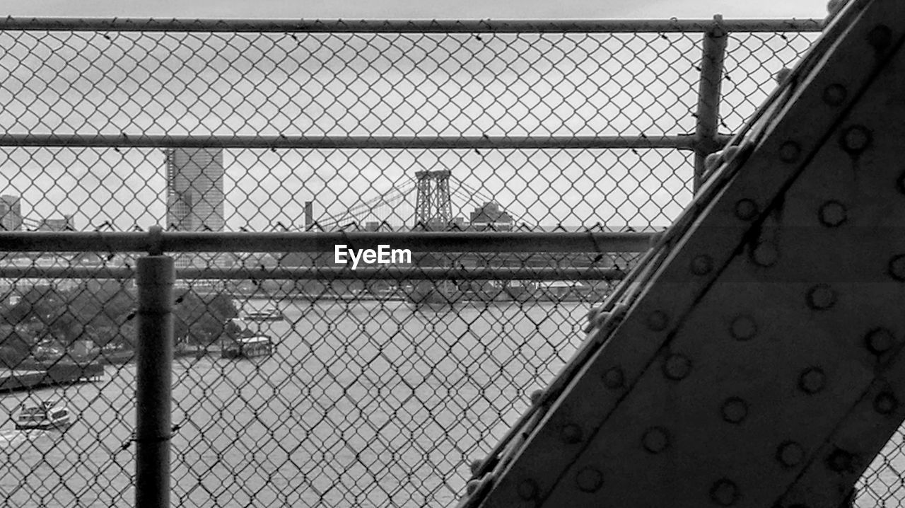 CLOSE-UP OF CHAINLINK FENCE AGAINST SKY SEEN THROUGH METAL GRATE