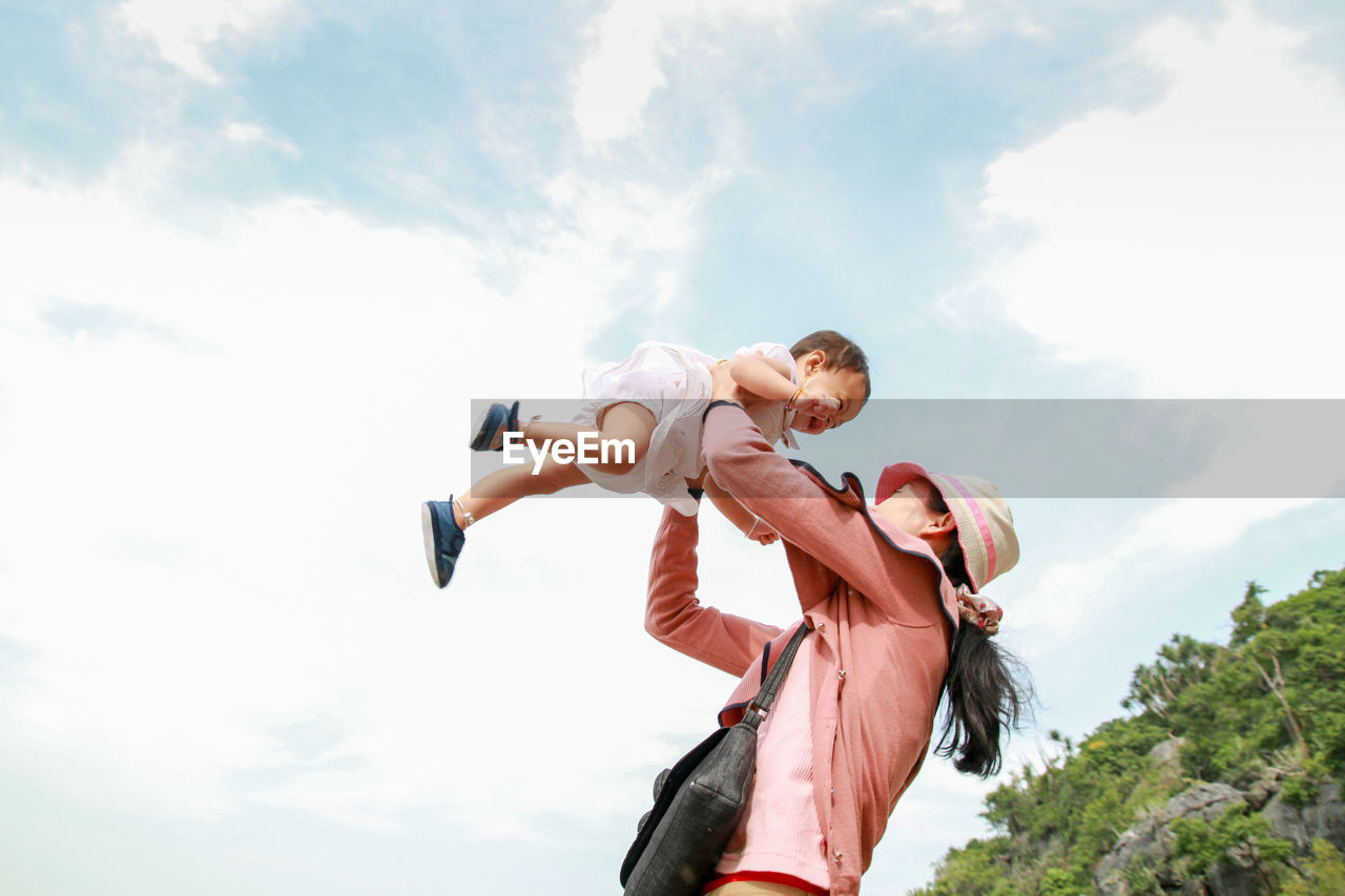 Low angle view of mother carrying daughter against sky