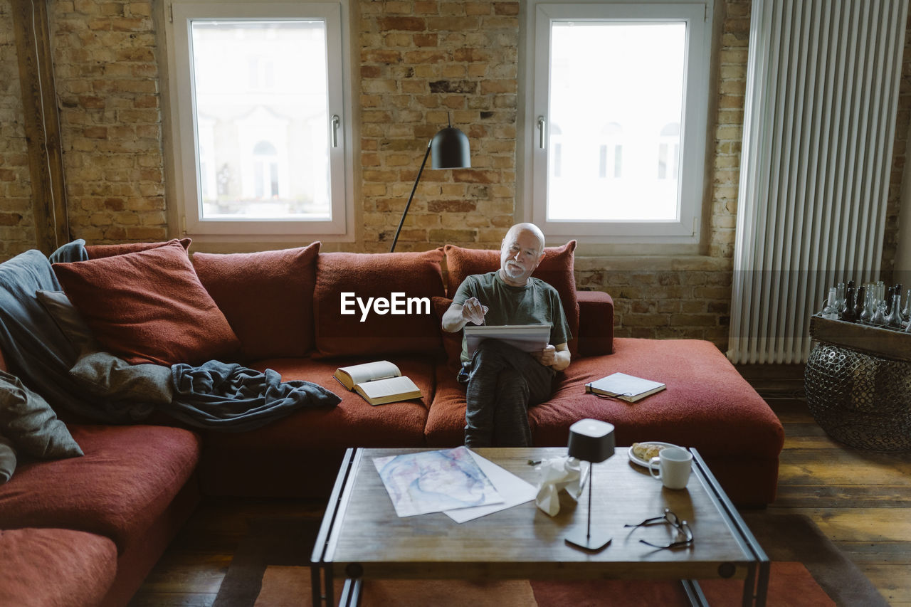 Senior man doing painting while sitting on sofa in living room at home