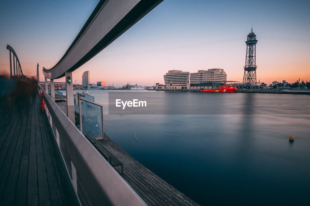 Bridge over river by buildings against sky during sunset