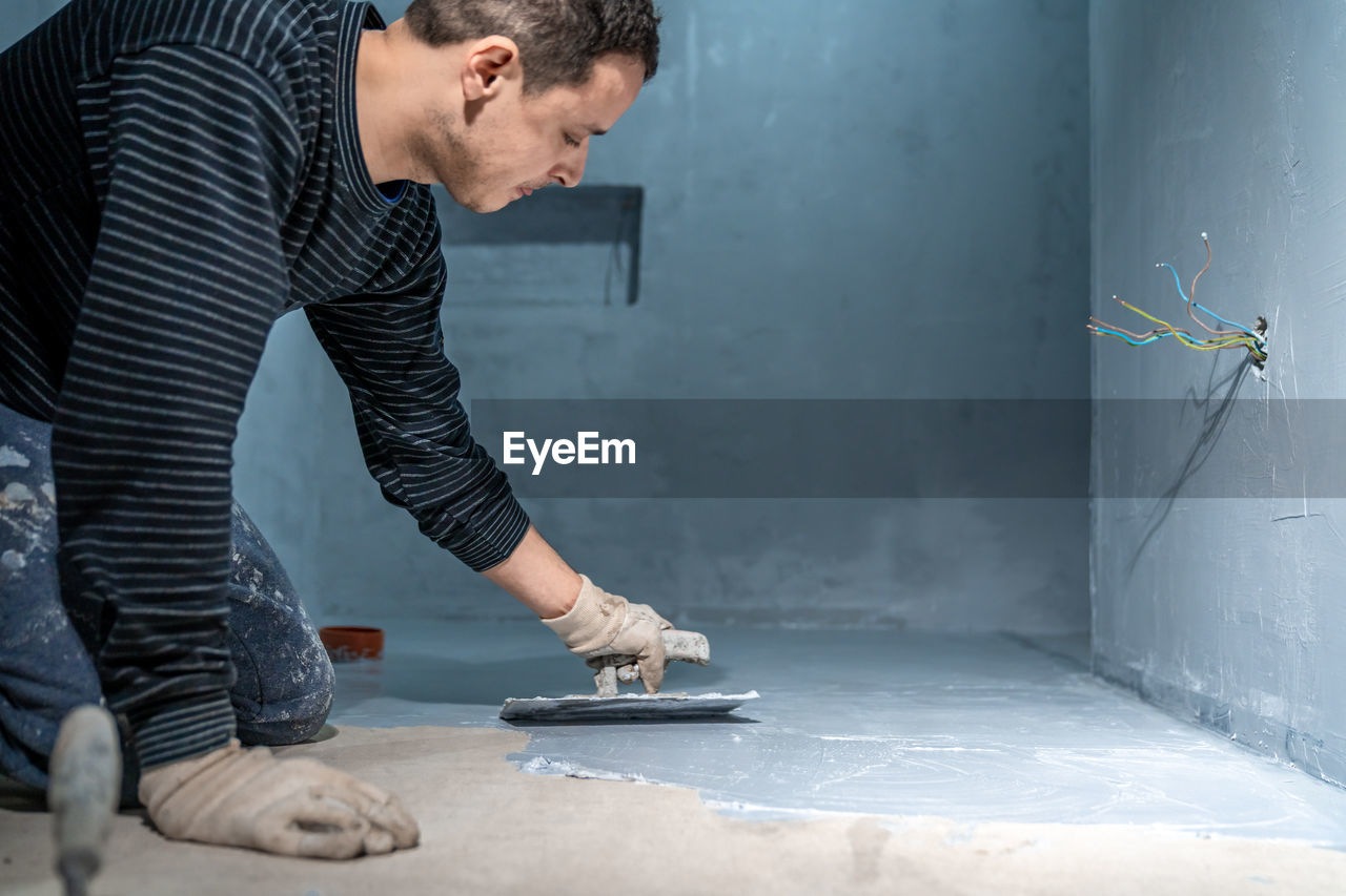 one person, adult, men, indoors, occupation, working, person, floor, casual clothing, standing, clothing, manual worker, creativity, side view, skill, young adult, cleaning, business, bending