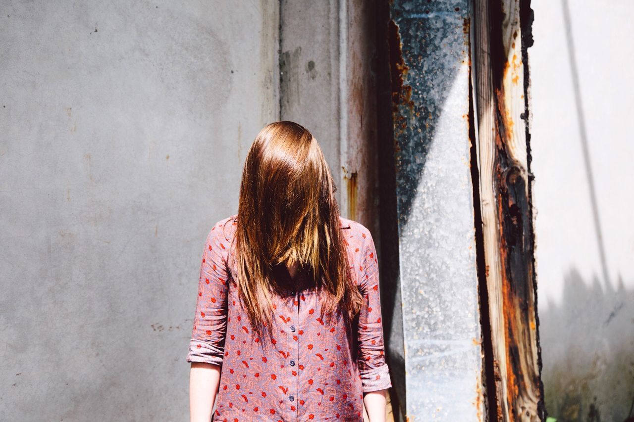 Woman with covered face standing against wall